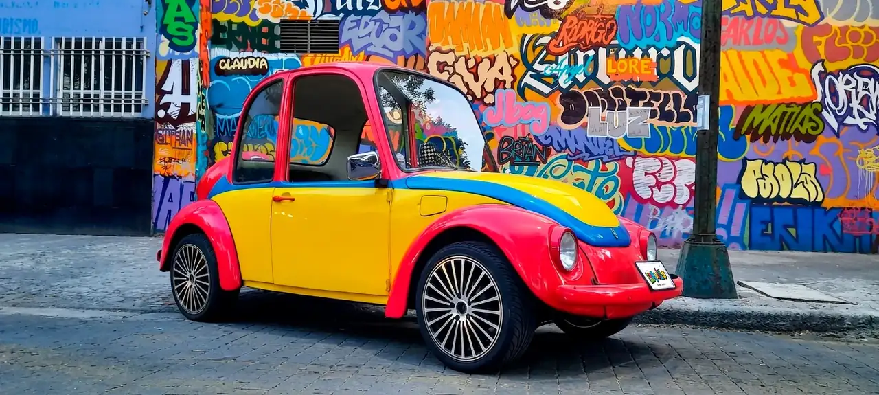 Vochito amarillo y fucsia del Payaso Loquillo frente a grafiti en Ciudad de México